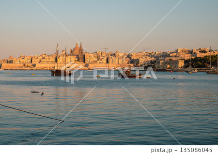 A breathtaking view of Valletta's historic skyline from the sea, showcasing its grand limestone buildings, fortifications, and domes under the Mediterranean sun. A breathtaking view of Valletta's historic skyline from the sea, showcasing its grand limestone buildings, fortifications, and domes under the Mediterranean sun. 135086045