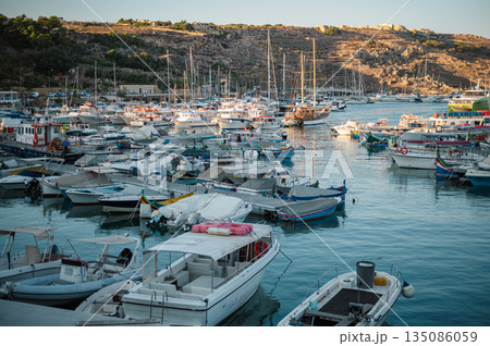 A stunning panoramic view of Mgarr Bay, showcasing the town, harbor, and ferries docking at the eastern end of Gozo, Malta, under the Mediterranean sky. A stunning panoramic view of Mgarr Bay, showcasing the town, harbor, and ferries docking at the eastern end of Gozo, Malta, under the Mediterranean sky. 135086059