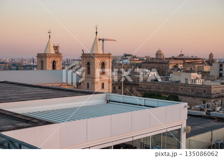 A stunning aerial view of Valletta's rooftops, showcasing the city's historic architecture, domes, and limestone buildings under the Mediterranean sky. A stunning aerial view of Valletta's rooftops, showcasing the city's historic architecture, domes, and limestone buildings under the Mediterranean sky. 135086062