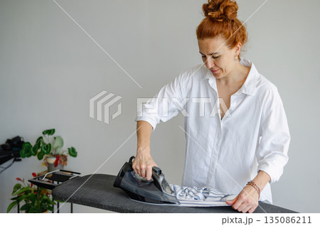 Young woman using ironing board to press clothes neatly at home. 135086211