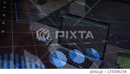 Holding stylus, businesswoman analyzing charts on business laptop at office desk, with smartphone 135086236