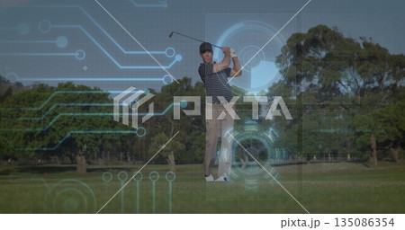 Swinging golfer in striped polo, khaki pants hitting ball on fairway, with club, glove, HUD overlay 135086354