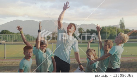 Adult coach coaching team in matching shirts gathering on sports field, with clipboard and watch Adult coach coaching team in matching shirts gathering on sports field, with clipboard and watch 135086368