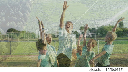Cheering coach and players raising arms on soccer pitch, with goal net metal fence matching jerseys 135086374