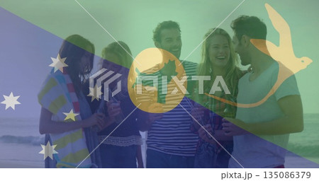 Friends in swimwear holding beer bottles on sandy beach, with towel and Australian flag graphic 135086379