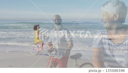 Three-generation family cycling and standing on beach, smiling with pink cruiser and black bicycles Three-generation family cycling and standing on beach, smiling with pink cruiser and black bicycles 135086396
