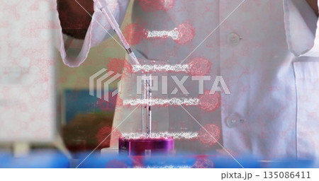 Scientist wearing lab coat, gloves dispensing liquid with pipette into purple test tube rack in lab 135086411