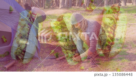 Woman in knit beanie, fleece top tying guy line at forest campsite, with tent stakes Woman in knit beanie, fleece top tying guy line at forest campsite, with tent stakes 135086448