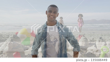 Father wearing denim shirt and white tee standing on sandy shore, with kids walking by sandcastle Father wearing denim shirt and white tee standing on sandy shore, with kids walking by sandcastle 135086449