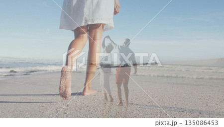 Walking woman's bare feet in white sundress on beach with ocean waves, dancing couple by headland 135086453