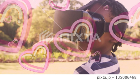 Boy exploring virtual world wearing headset in sunlit garden, with pink heart overlays, copy space 135086469