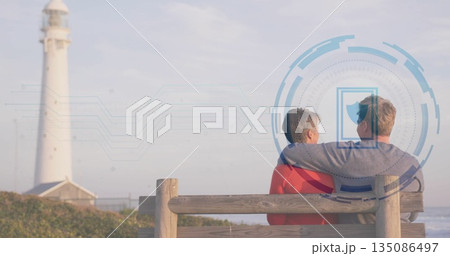 Sitting couple embracing on bench coastal path, with lighthouse and shield overlay, copy space 135086497