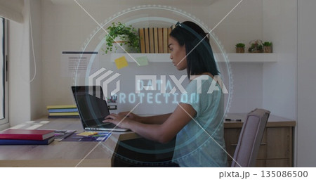 Typing woman wearing gray t-shirt at home office with laptop, data protection overlay, copy space 135086500