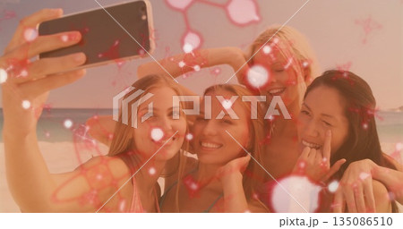 Smiling group of women in colorful bikinis holding smartphone for beach selfie with sparkle overlay Smiling group of women in colorful bikinis holding smartphone for beach selfie with sparkle overlay 135086510