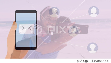 Connecting smartphone with envelope icon to couple using phone on beach via profiles, copy space Connecting smartphone with envelope icon to couple using phone on beach via profiles, copy space 135086533