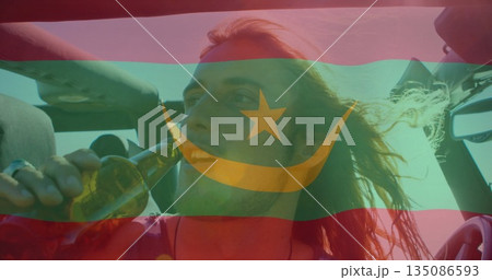 Drinking man in sleeveless top raising glass bottle in convertible car, with crescent-star theme 135086593