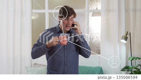 Talking on smartphone, man gesturing in living room with frosted window, digital connection icons 135086594