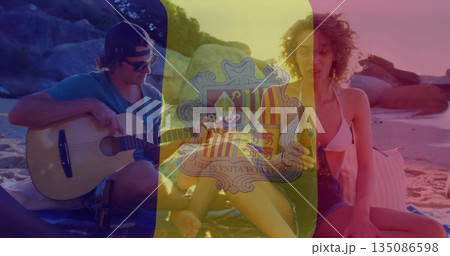 Strumming acoustic guitar and ukulele, friends in swimwear sharing bottled drink on beach blanket 135086598