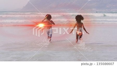 Running siblings splashing into shallow ocean at beach, wearing pink bikini and blue swim trunks 135086607