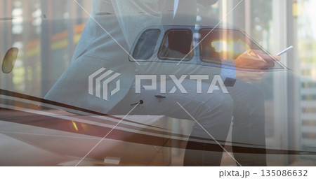 Holding smartphone and stylus, executive in suit leaning on jet wing in hangar, with tinted window Holding smartphone and stylus, executive in suit leaning on jet wing in hangar, with tinted window 135086632