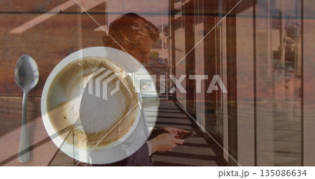 Business executive in blazer checking messages on smartphone in corridor, with coffee cup and spoon Business executive in blazer checking messages on smartphone in corridor, with coffee cup and spoon 135086634