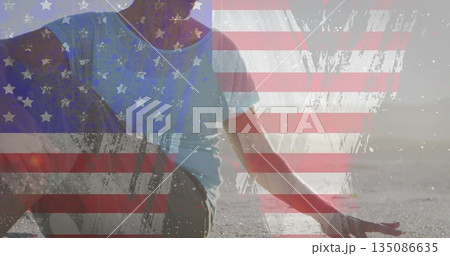 Sitting senior woman in T-shirt and leggings doing yoga on beach at sunset, with flag overlay Sitting senior woman in T-shirt and leggings doing yoga on beach at sunset, with flag overlay 135086635