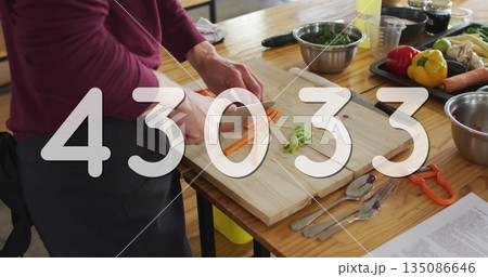 Chopping cook slicing carrots on wood cutting board at kitchen counter wearing apron, copy space Chopping cook slicing carrots on wood cutting board at kitchen counter wearing apron, copy space 135086646