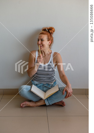 Portrait of a thoughtful girl holding a pen and notebook, looking aside, searching for inspiration. 135086666