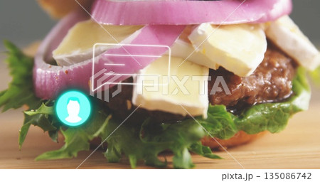 Displaying gourmet burger with cheese and onion rings on wooden board, with comment interface icons 135086742