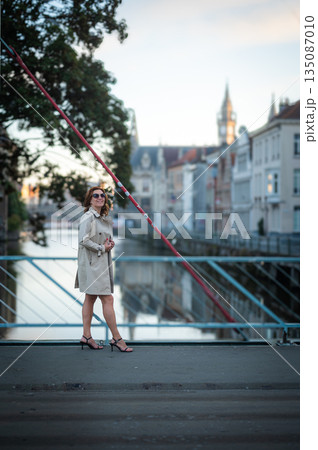 Elegant, well-groomed woman with fashionable style strolling around the city in a beige coat and sunglasses. Looking confident and sophisticated. Elegant, well-groomed woman with fashionable style strolling around the city in a beige coat and sunglasses. Looking confident and sophisticated. 135087010
