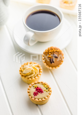 Sweet mini tartlets and coffee cup on white table. Sweet mini tartlets and coffee cup on white table. 135087116