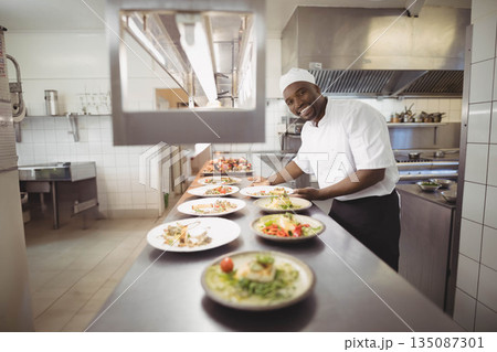 African American male chef arranging dishes under heating lamp on steel kitchen counter, copy space 135087301