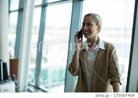 Female business traveler talking on smartphone at airport by suitcase, glass windows, copy space Female business traveler talking on smartphone at airport by suitcase, glass windows, copy space 135087409