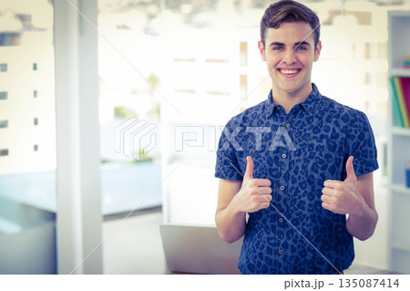 Man wearing blue short-sleeve shirt giving double thumbs-up at office desk with laptop, copy space 135087414