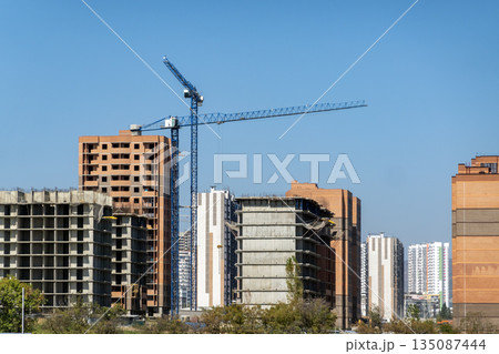 New residential district under construction in Novorossiysk, Russia, with unfinished monolithic apartment buildings and tower cranes against the sky 135087444