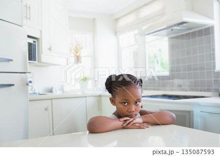 Child African American girl leaning on island looking thoughtful in kitchen near white cabinets Child African American girl leaning on island looking thoughtful in kitchen near white cabinets 135087593