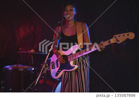 African American woman musician performing on stage singing into microphone and playing bass guitar 135087606