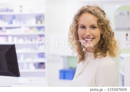 Female pharmacy staff smiling while checking computer monitor and organizing shelves, copy space Female pharmacy staff smiling while checking computer monitor and organizing shelves, copy space 135087609