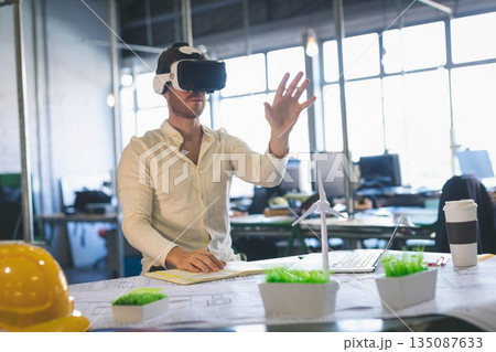 Virtual reality headset resting among blueprints laptop wind turbine model on desk in modern office Virtual reality headset resting among blueprints laptop wind turbine model on desk in modern office 135087633