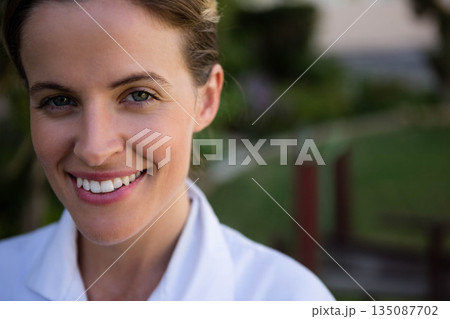 Woman smiling broadly in white collared coat outdoors in home garden with wooden posts Woman smiling broadly in white collared coat outdoors in home garden with wooden posts 135087702
