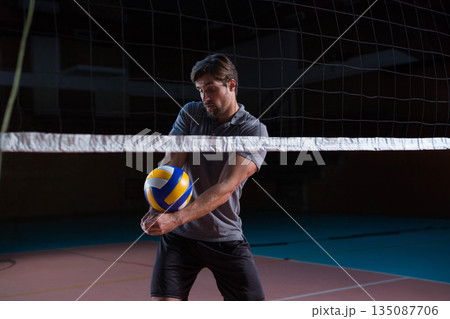 Man performing forearm pass on gym volleyball court over net with yellow blue white volleyball 135087706