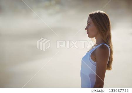Woman wearing white tank top standing at shoreline, facing right and watching waves, copy space Woman wearing white tank top standing at shoreline, facing right and watching waves, copy space 135087733