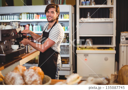 Male barista operating espresso machine behind counter in café with coffee cup and pastries Male barista operating espresso machine behind counter in café with coffee cup and pastries 135087745