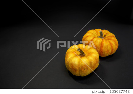 Two bright orange pumpkins arranged on a black background. Minimalistic autumn still life with strong contrast, perfect for harvest, Halloween, and seasonal themes. 135087748