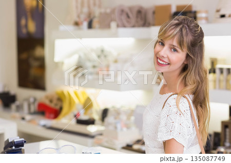 Woman in mid 20s smiling and looking over shoulder at boutique counter with eyeglasses, copy space 135087749