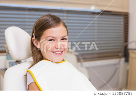 Female child patient sitting in dental clinic chair wearing bib smiling and waiting for care Female child patient sitting in dental clinic chair wearing bib smiling and waiting for care 135087785