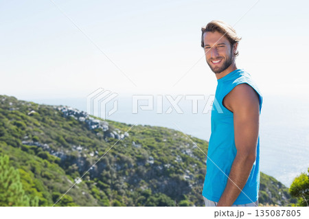 Male wearing blue sleeveless shirt standing on coastal hillside smiling at sea horizon, copy space 135087805