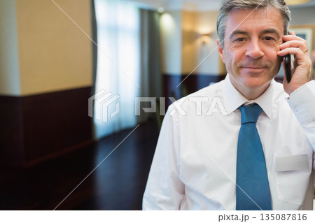 Mature man standing in hotel corridor holding smartphone and conference badge, copy space Mature man standing in hotel corridor holding smartphone and conference badge, copy space 135087816
