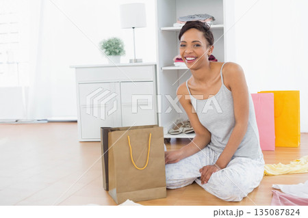 African American woman smiling while handling brown paper bag sitting in bedroom with gift bags African American woman smiling while handling brown paper bag sitting in bedroom with gift bags 135087824