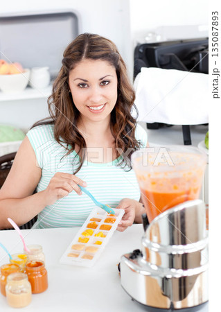Woman standing behind kitchen counter using pastel blue spoon filling sectioned tray with purees Woman standing behind kitchen counter using pastel blue spoon filling sectioned tray with purees 135087893